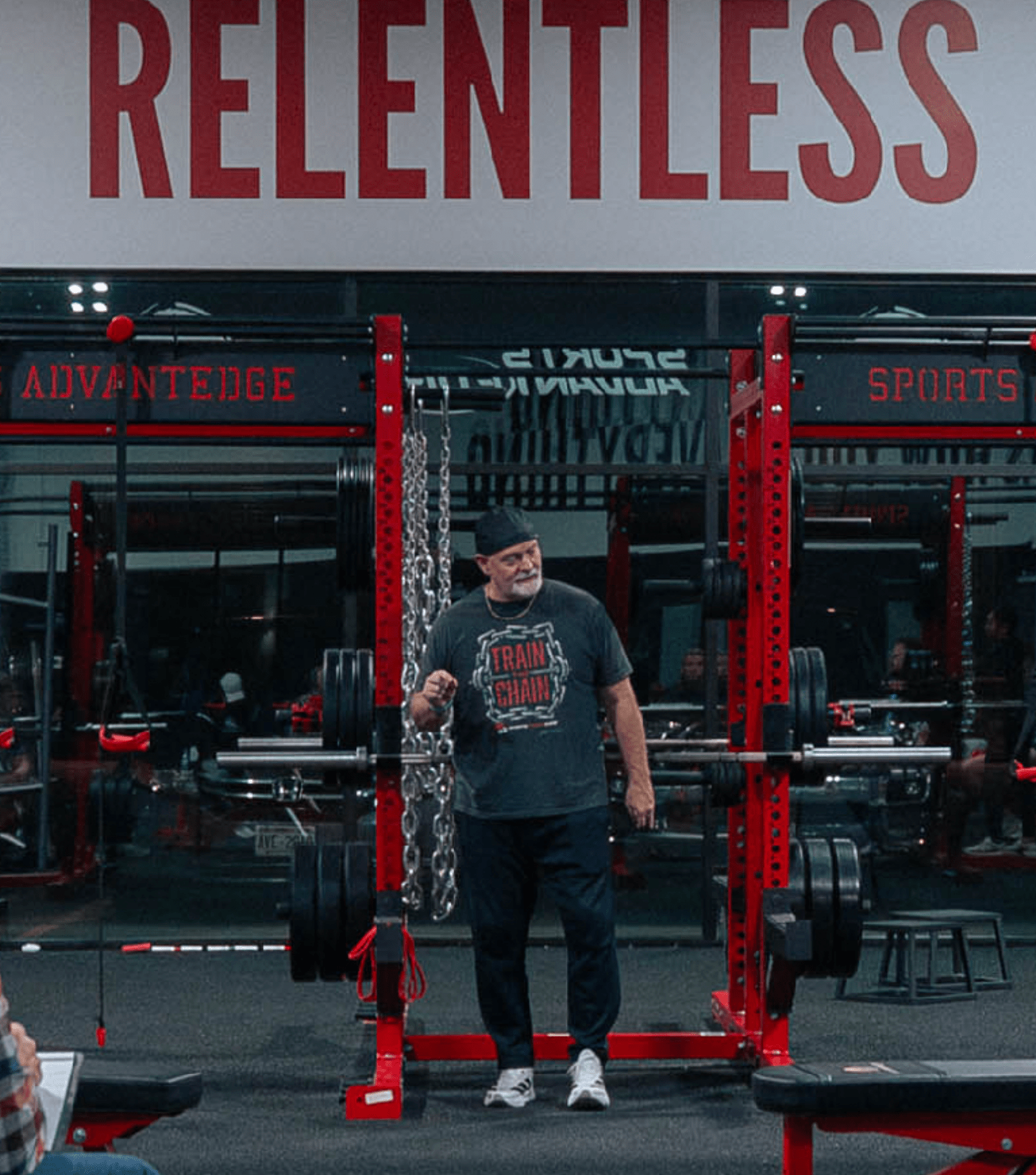 Man lifting weights in a gym with 'Relentless' and 'Advantage Sports' branding.